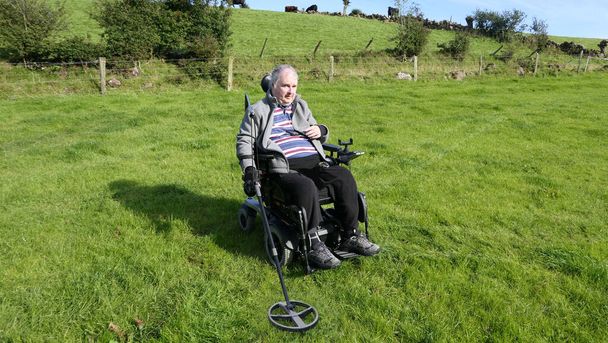 Hombre discapacitado Usuario de silla de ruedas Detección de metales para monedas en un campo - Foto, Imagen