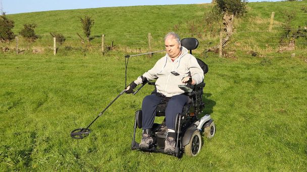 Disabili uomo sedia a rotelle metal detecting per monete in un campo - Foto, immagini