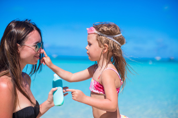 Маленька дівчинка наносить крем для сонячних променів на ніс мами
 - Фото, зображення