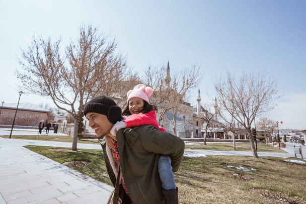 father carrying her daughter on his shoulder piggyback ride while visiting mosque in the city of konya turkey - Photo, image
