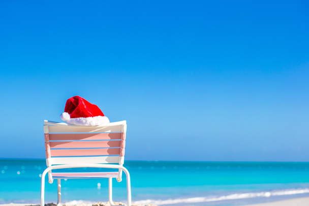 Nahaufnahme roter Weihnachtsmann auf Stuhllehne am tropischen Strand - Foto, Bild