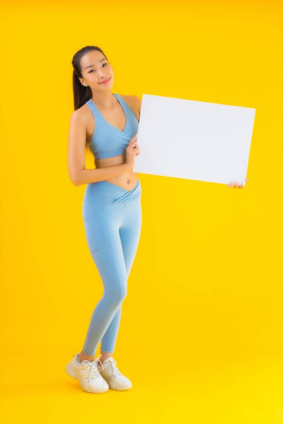 Портрет красива молода азіатка в спортивному одязі показує порожній білий рекламний щит на жовтому ізольованому фоні
 - Фото, зображення
