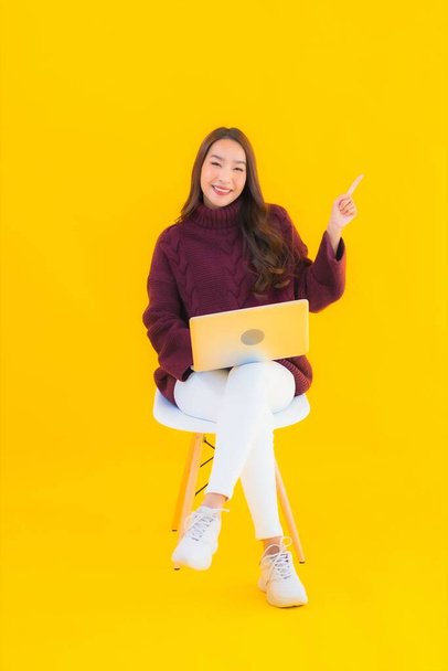 Retrato hermosa joven asiática mujer uso ordenador portátil en amarillo aislado fondo - Foto, imagen