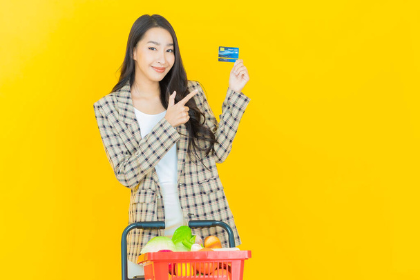 Renkli arka planda süpermarketten alınmış market sepetiyle gülümseyen güzel Asyalı kadın portresi. - Fotoğraf, Görsel