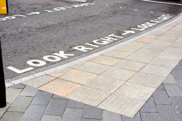 Tactile tiles for the blind. Panels for the blind laid on asphalt. Guide tape for the disabled. the inscription look right at the pedestrian crossing. - Foto, Imagem