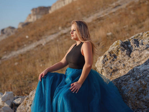 Fashionable woman on desert field near mountain wearing black top and blue tulle skirt. Wild west. Summer holidays dance. Beautiful and sexy plus size model - Photo, Image