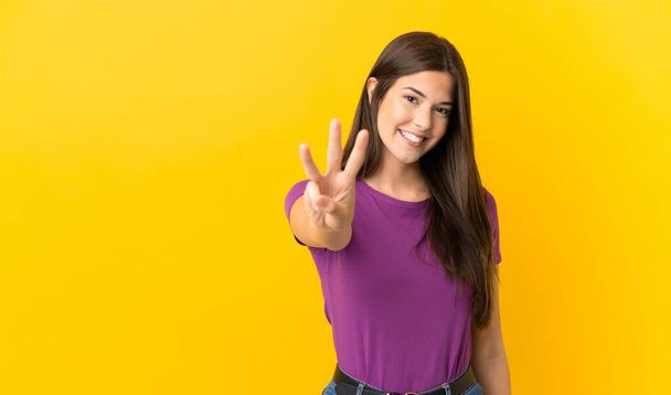 Teenager Brazilian girl over isolated yellow background happy and counting three with fingers - Fotó, kép