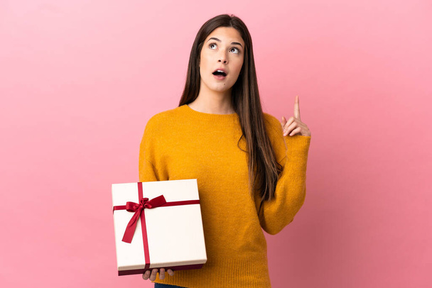 Teenager Brazilian girl holding a gift over isolated pink background thinking an idea pointing the finger up - Фото, зображення
