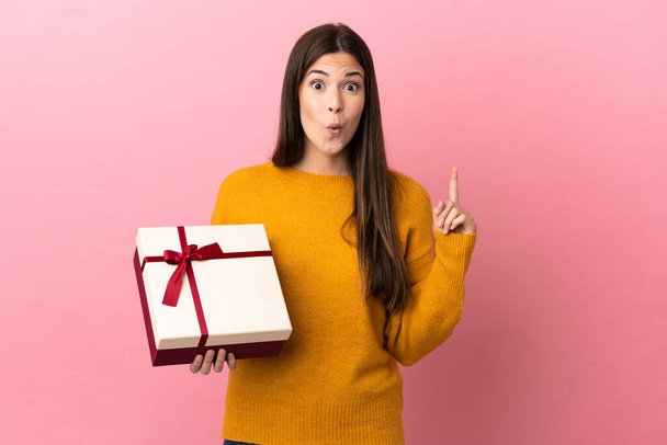 Teenager Brazilian girl holding a gift over isolated pink background intending to realizes the solution while lifting a finger up - Фото, зображення