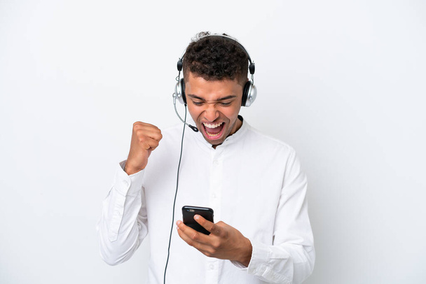 Telemarketer Brazilian man working with a headset isolated on white background with phone in victory position - Foto, Bild