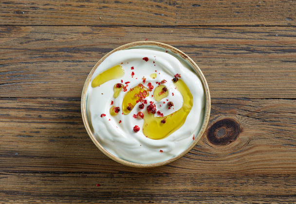bowl of sour cream or greek yogurt decorated with olive oil and red pepper on wooden kitchen table, top view - Valokuva, kuva