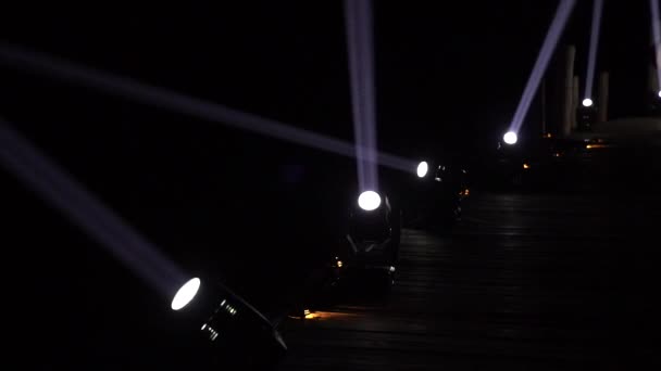Spotlight machines create light beams with moving its direction in the dark night on walking wood way - Felvétel, videó