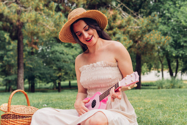 Жінка грає на укулеле на пікніку з друзями в природі, співаючи пісню. Хіпі жінка грає музику зі своїми друзями під час кемпінгу
. - Фото, зображення