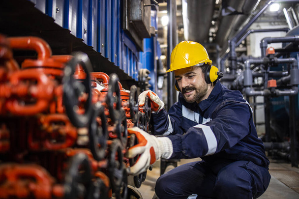 Industrial worker in power plant or heating plant controlling pressure in pipe valves in factory. - Foto, Bild