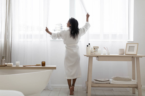 "Приваблива чорна жінка" відкриває завіси, коли готується ранкова красуня "У ванній кімнаті" , "Посміхнена афроамериканська жінка, яка носить білу халат", готуючись до спа - лікування вдома ". - Фото, зображення