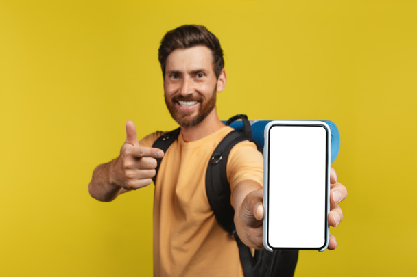 Щасливий чоловік з рюкзаком, що показує сучасний смартфон з білим порожнім екраном, макет, копіювання простору. Онлайн бронювання турів та концепція польоту
 - Фото, зображення