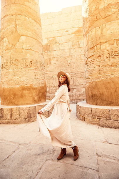 Happy woman traveler explores the ruins of the ancient Karnak temple in the heritage city of Luxor in Egypt. Giant row of columns with carved hieroglyph - Foto, imagen