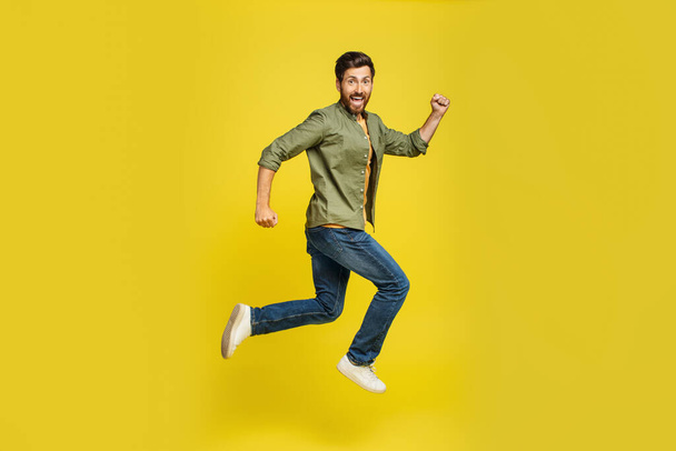 Portrait of middle aged man running over yellow background, side view shot of joyful male jumping in air, hurry up to sales or discounts, free copy space - Photo, image
