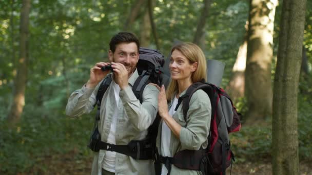 Exciting scene. Couple of two happy middle aged tourists travelling in woodland, looking forward through binoculars, enjoying view, slow motion, free space - Imágenes, Vídeo
