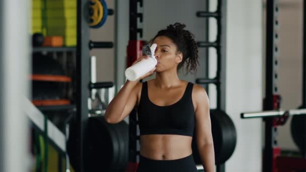 Sports and water balance. Young pretty african american woman athlete drinking water, hydrating body during workout at gym, slow motion, free space - Video, Çekim