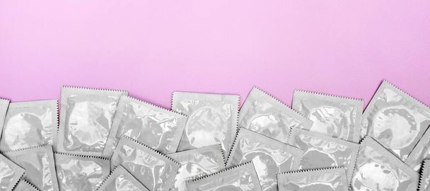 Many white packages of unopened condoms on a pink background. Using a condom to reduce the chance of pregnancy or sexually transmitted diseases, STDs. The concept of safe sex and reproductive health. - Zdjęcie, obraz