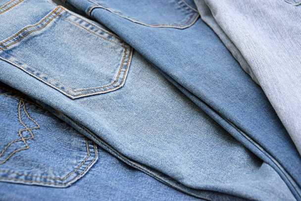 Lots of jeans pants in a stack. Denim background. The concept of buying, selling, shopping and trendy modern clothes. - Foto, afbeelding