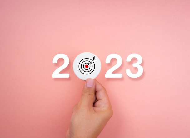 2023 Happy New year background banner. Two thousand Twenty-Three year numbers on pink background with hand holding target icon. Welcome, Merry Christmas, and business goals in 2023 year calendar. - Photo, image