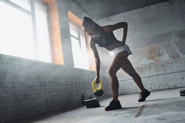 Full length of confident young African woman exercising with kettlebell in gym - Foto, Imagem