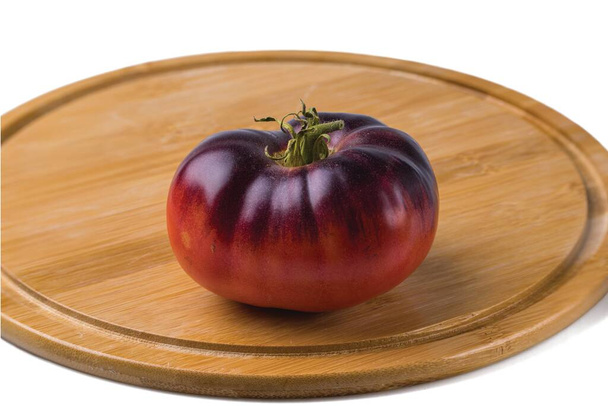 Close up view of ripe black variety of tomato on wooden cutting board isolated on white background. - Fotoğraf, Görsel