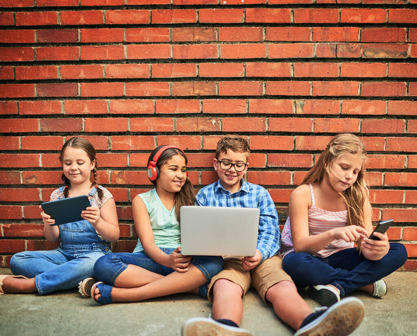 Its how we have fun. a group of young children using digital devices against a brick wall - Foto, Bild