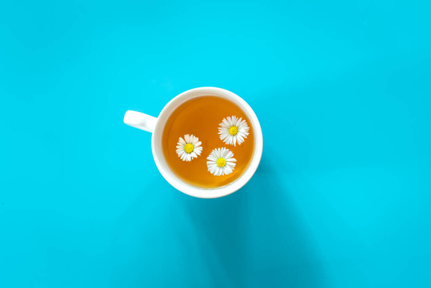 A cup of chamomile tea on a blue background, flat lay, minimalism. - Фото, зображення