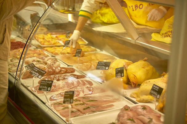 Milan, italy 20 august 2022: Shooting a scene at the market where you can see a fridge bench full of meat of various kinds, and the job that takes a piece to sell it to the customer. - Foto, Imagem