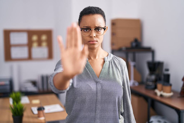 Afro-Amerikaanse vrouw die op kantoor werkt met een bril op, stop met zingen met handpalm van de hand. waarschuwingsuitdrukking met negatief en ernstig gebaar op het gezicht.  - Foto, afbeelding