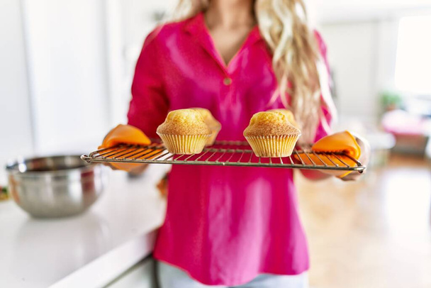 Молодая женщина держит духовку поднос с кексами на кухне - Фото, изображение