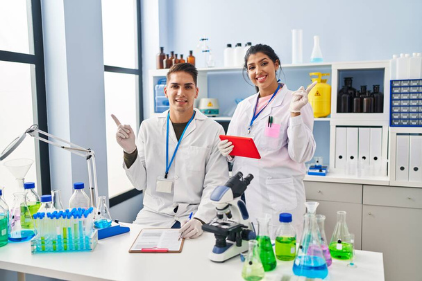 Fiatal orvosok dolgoznak a tudós laboratóriumban mosolyogva boldog mutogatás kézzel és ujjal oldalra  - Fotó, kép