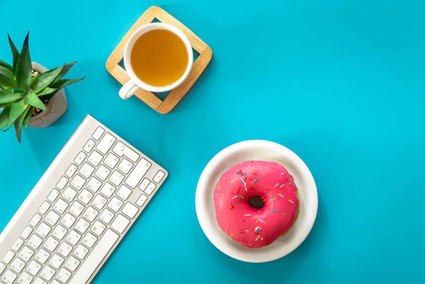 Пончик, чай и клавиатура на голубом фоне, плоская кладка, рабочее место и концепция творчества. - Фото, изображение
