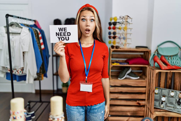 Young caucasian woman holding we need you banner hiring at retail shop scared and amazed with open mouth for surprise, disbelief face  - Fotó, kép