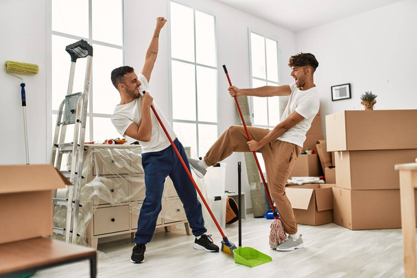 Two hispanic men couple cleaning and dancing at new home - Foto, Imagen