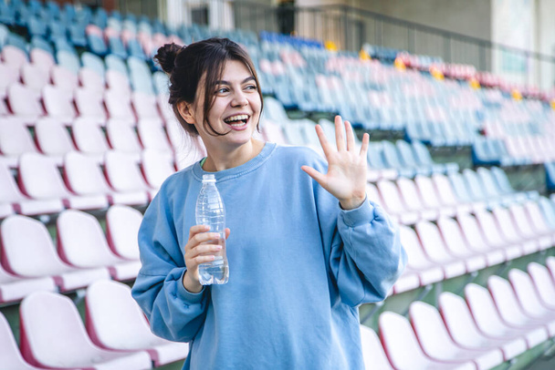 Attractive cheerful young woman sportswoman drinks water after training outdoors in the stadium. - Fotó, kép