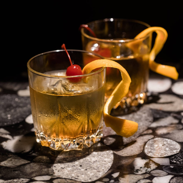 Two Old Fashioned cocktails garnished with curled orange peels and maraschino cherries. Square crop. - Foto, Bild