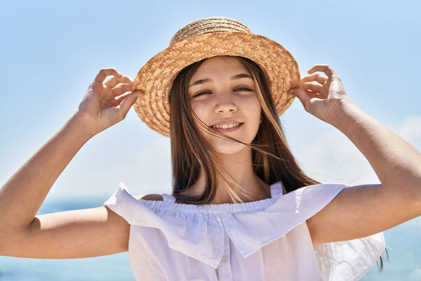 Αξιολάτρευτο κορίτσι τουρίστα χαμογελώντας αυτοπεποίθηση φορώντας καλοκαιρινό καπέλο στην παραλία - Φωτογραφία, εικόνα