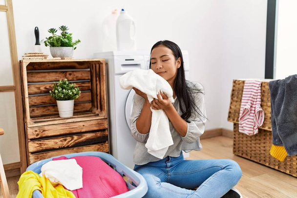 Giovane donna latina sorridente fiducioso odore di vestiti in lavanderia - Foto, immagini