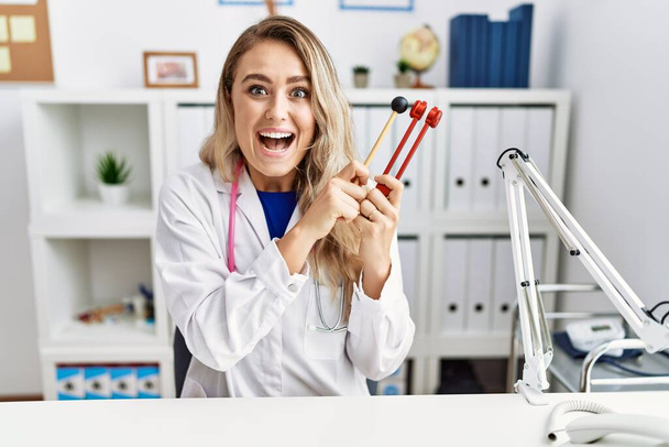 Young beautiful doctor woman holding diapason instrument celebrating crazy and amazed for success with open eyes screaming excited.  - Foto, afbeelding