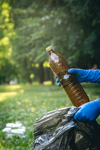 Чоловік кладе пластикову пляшку в мішок для сміття, концепцію прибирання лісів і любов до природи
. - Фото, зображення