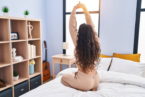 Giovane donna ispanica svegliarsi braccia tese seduto sul letto in camera da letto - Foto, immagini