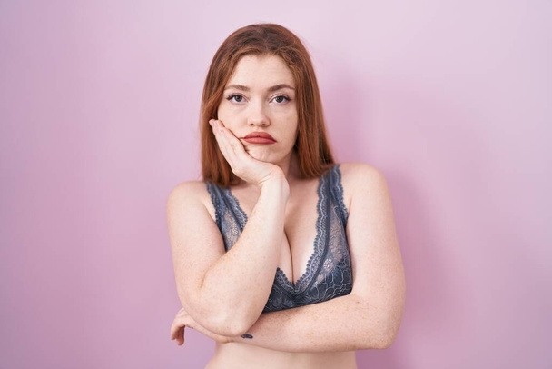 Redhead woman wearing lingerie over pink background thinking looking tired and bored with depression problems with crossed arms.  - Photo, image