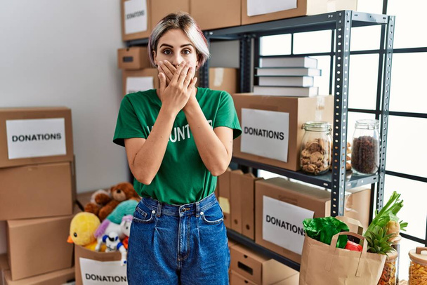 Young beautiful woman wearing volunteer t shirt at donations stand shocked covering mouth with hands for mistake. secret concept.  - Foto, Imagem