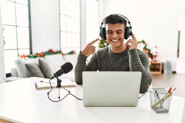 Hombre hispano guapo grabando podcast sonriendo feliz señalando con la mano y el dedo  - Foto, imagen