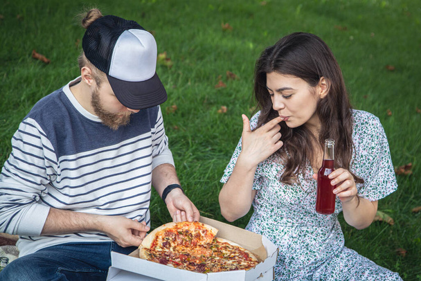 A young man and woman eating pizza together, picnic and dating concept in nature. - Foto, Imagem