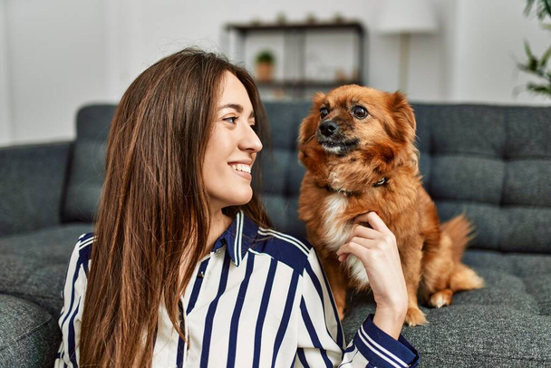Young hispanic woman smiling confident sitting on floor with dog at home - Foto, imagen
